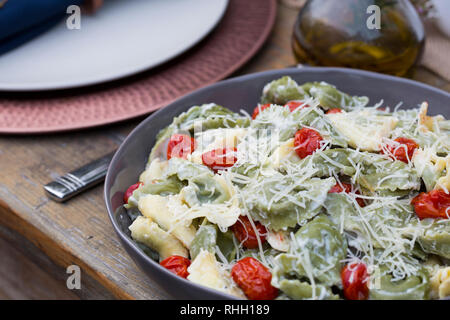 Servierschale von Grün und Gelb Ravioli mit Tomaten und geriebenem Parmesan auf hölzernen Tisch für Hinterhof outdoor Dinner Party. Stockfoto