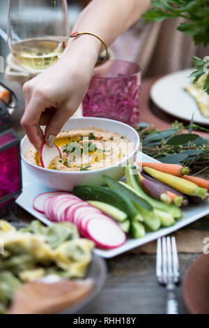 Weibliche Hände eintauchen Rettich in Schale, Hummus Dinner Party im Freien. Stockfoto