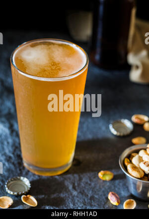 Pint Glas Handwerk Weißbier auf schiefer bar Oberfläche mit Verschlusskappen und Pistazien. Stockfoto