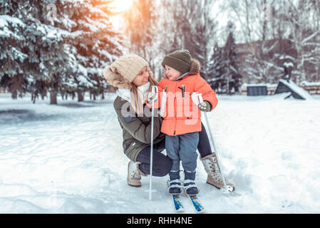 Junge glückliche Mutter, hält eine Frau einen Jungen 2-4 Jahre alten Sohn, lernt, um Ski zu fahren. Im Winter im Park. Freier Platz für Text. Pflege für Baby, die ein Stockfoto