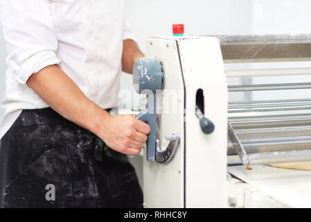 Baker mit ausrollmaschine Maschine Croissants zu produzieren Teig bei der Bäckerei. Stockfoto