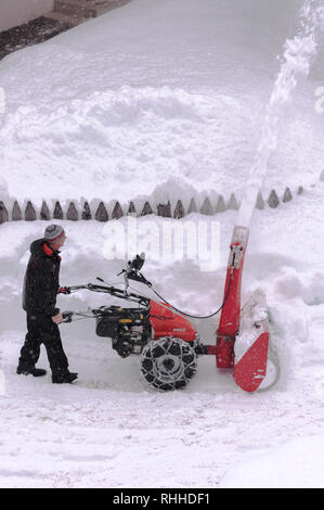 Der Mensch nimmt den Schnee mit einem Schneepflug, hohe Schnee auf den Seiten Stockfoto