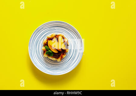 Belgische Waffel in der Platte mit Schokolade und Pfirsich auf gelbem Hintergrund flach Stockfoto