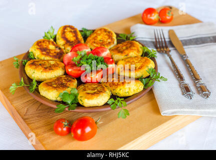 Hausgemachte ruddy Käse Kartoffeln und Schnitzel, mit frischen Tomaten und Petersilie dekoriert, in Keramik Platte auf einem Holzbrett Stockfoto