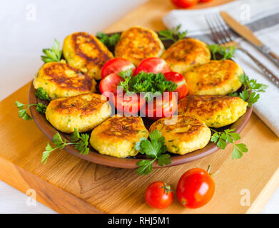 Hausgemachte ruddy Käse Kartoffeln und Schnitzel, mit frischen Tomaten und Petersilie dekoriert, in Keramik Platte auf ein Brett aus Holz Stockfoto