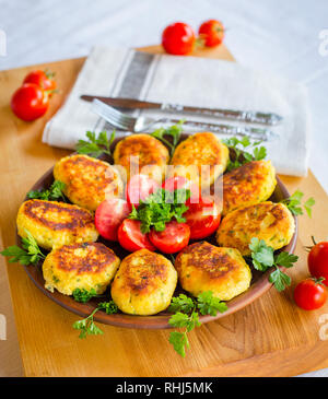 Hausgemachte ruddy Käse Kartoffeln und Schnitzel, mit frischen Tomaten und Petersilie dekoriert, in Keramik Platte auf ein Brett aus Holz Stockfoto