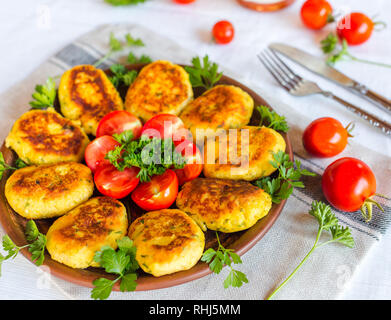Hausgemachte ruddy Käse Kartoffeln und Schnitzel, mit frischen Tomaten und Petersilie dekoriert, in Keramik Platte auf eine Serviette Stockfoto