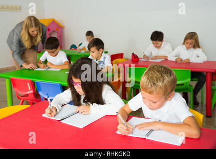 Schoolkids am Schreibtisch in Klassenzimmer und Lehrer helfen arbeiten Stockfoto