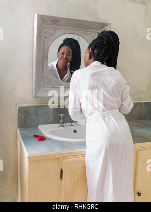 Hübsche junge afrikanische amerikanische Frau, die Ihre morgendliche Routine zu tun vor dem Badezimmerspiegel Stockfoto