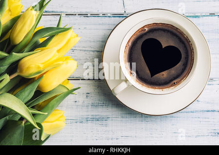Top of view cup form coffee with heart and spring tulips on wooden table. Stockfoto
