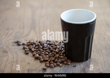 Tasse Kaffee am Tisch von Kaffeebohnen umgeben Stockfoto