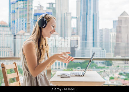 Junge Frau lehrt eine Fremdsprache lernt eine Fremdsprache im Internet auf ihrem Balkon vor dem Hintergrund einer großen Stadt. Online Sprache Stockfoto