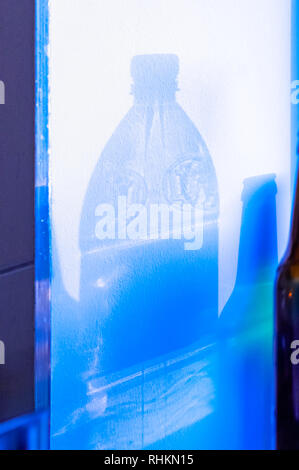 Projektion der transparente Schatten eines leeren Kunststoff Flasche Wasser und eine leere Flasche Bier auf einer weißen Wand Stockfoto