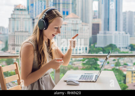 Junge Frau lehrt eine Fremdsprache lernt eine Fremdsprache im Internet auf ihrem Balkon vor dem Hintergrund einer großen Stadt. Online Sprache Stockfoto