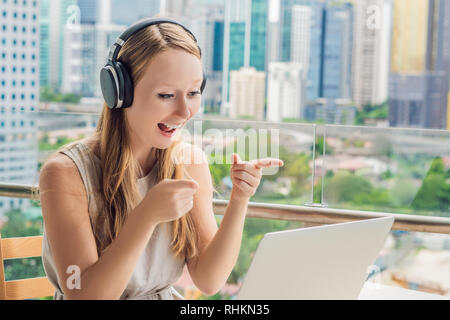 Junge Frau lehrt eine Fremdsprache lernt eine Fremdsprache im Internet auf ihrem Balkon vor dem Hintergrund einer großen Stadt. Online Sprache Stockfoto