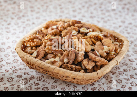 Frische Walnüsse in einer rattan Korb, auf einem weißen blumige Tischdecke geschält Stockfoto