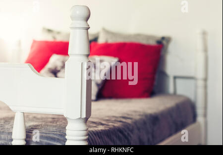Weiß aus Holz geschnitzte Bett mit grauen Bettdecken und Kissen rot Stockfoto