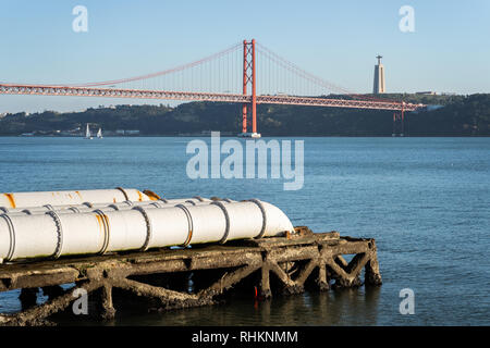 Industrielle weiße Rohre in der Nähe Central Tejo in Lissabon, die in den Fluss Tejo, Christus König und Brücke im Hintergrund, Portugal Stockfoto