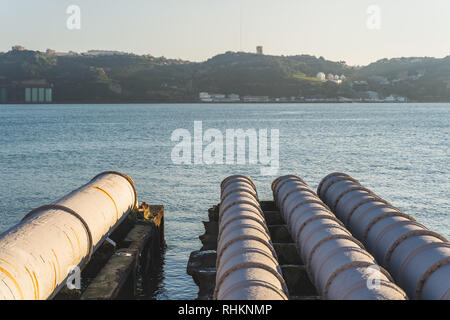 Industrielle weiße Rohre in der Nähe Central Tejo in Lissabon, die in den Fluss Tejo, Christus König und Brücke im Hintergrund, Portugal Stockfoto