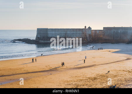 Fort in Torre Strand, blauer Himmel und Ozean Wellen, gelb braun Sand, Menschen zu Fuß in den Sand. Niedrige sun, Fort werfen Schatten auf dem Sand. Stockfoto