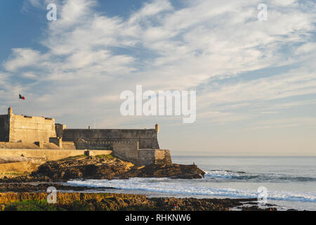 Blick auf Saint Julian Festung mit Leuchtturm Turm vom Strand (Praia) von Carcavelos, Portugal. Wellen aus dem Atlantik, Strand und erodierten Felsen. Stockfoto