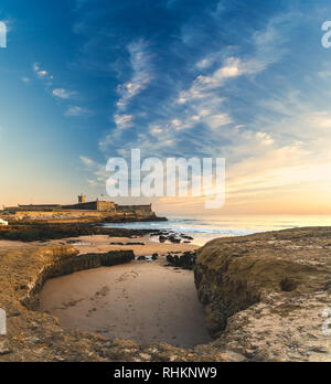 Blick auf Saint Julian Festung mit Leuchtturm Turm vom Strand (Praia) von Carcavelos, Portugal. Wellen aus dem Atlantik, Strand und erodierten Felsen. Stockfoto