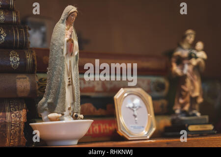 Statue von Maria, der Mutter Jesu, nach dem Neuen Testament und den Koran sitzen auf einem alten Regal mit sehr alten Büchern gefüllt. Stockfoto