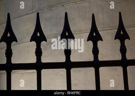 Silhouette der gezackten Zaunpfosten gegen eine Wand mit Hintergrundbeleuchtung Stockfoto