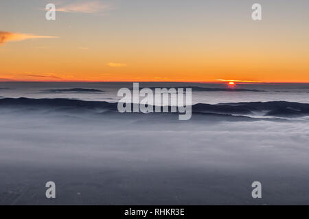 Schönen Sonnenuntergang über einem Tal im Nebel mit Bergen und Hügeln gefüllt Stockfoto