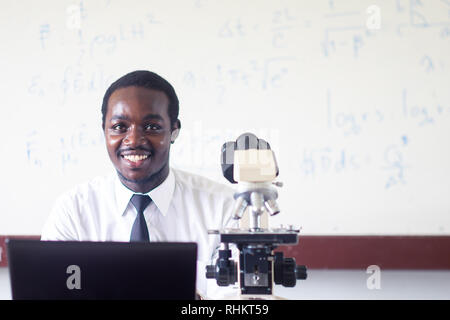 Afrikanische Wissenschaft Lehrer Lehre und lächelnd im Mint-Klasse mit Mikroskop und Computer. Stockfoto
