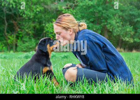 Junge kaukasier Hündin Besitzer küsse Rottweiler Welpen auf den Kopf in natürlichen Wiese Stockfoto