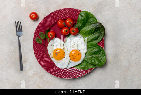 Zwei Spiegeleier in Herzform mit Romano Salat und Tomaten an der roten Platte mit Gabel auf weißem Hintergrund. Horizontale Konzept der gesunde italienische fo Stockfoto