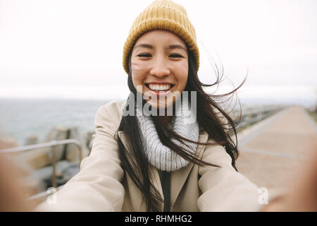 Freundliche asiatische Frauen stehen im Freien an einem Wintermorgen mit offenen Armen. Lächelnde Frau im Winter Kleidung stehen im Freien an einem kalten Tag. Stockfoto