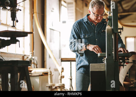Reife männliche Tischler arbeiten an bandsäge Maschine in der Schreinerei. Ältere Menschen Schneiden von Holz auf der Maschine. Stockfoto