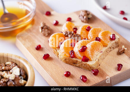 Sandwich mit Granatapfel Getreide, Honig, Nüsse und Mandarinen auf weißen Hintergrund. Roh essen. Gesunde Lebensmittel für Frühstück oder Mittagessen. Selektive konzentrieren. Stockfoto