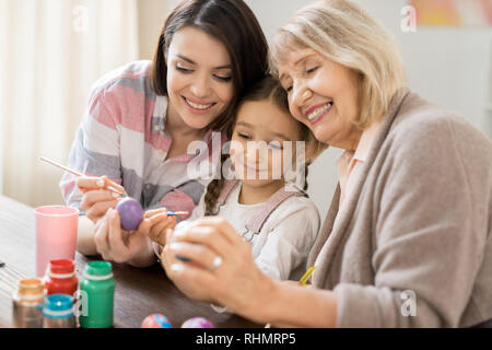 Glückliche kleine niedliche Mädchen, ihre Mutter und Großmutter looknig an einem der bemalte Ostereier Stockfoto