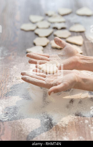 Hände von Frau einer der Rohstoffe Cookies in Form von Herzen halten beim Kochen hausgemachte Backwaren Stockfoto
