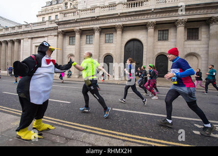 Eine Frau, gekleidet wie ein Pinguin high-fives Läufer, wie sie die Bank von England, in der City von London, während des Cancer Research UK London Winter ausgeführt werden. Stockfoto
