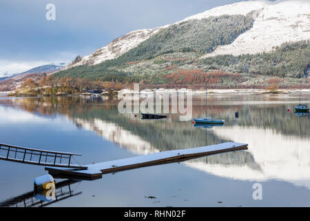 Reflexionen in Loch Leven mit Steg und Boote an einem kalten Wintermorgen von Glencoe Dorf, Highlands, Schottland Stockfoto