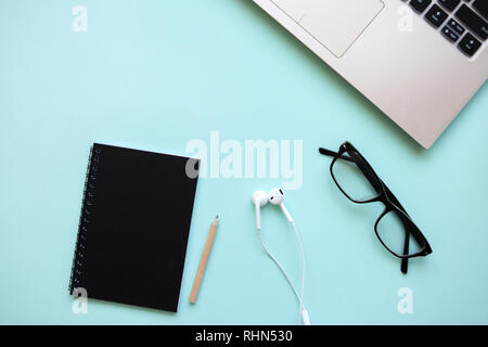 Arbeitsbereich in einem trendigen Blau. Viele verschiedene Dinge wie einen Laptop und Kopfhörer sind auf dem Tisch. Stockfoto