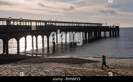 Boscombe, Dorset, Großbritannien. 3. Februar 2019. UK Wetter: Am frühen Morgen Läufer Joggen am Strand entlang in Boscombe. Der berühmte Pier gegen die helle Morgensonne im Englischen Küstenort Boscombe Silhouette. Credit: DWR/Alamy leben Nachrichten Stockfoto