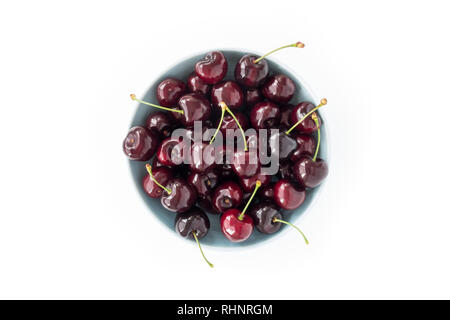 Blick von oben auf eine blaue Schale mit frischen Kirschen auf weißem Hintergrund gefüllt. Stockfoto