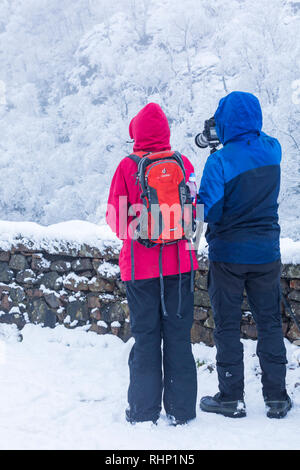 Paar stehend mit Menschen machen Fotos der Winterlandschaft Schnee und Raureif an Rannoch Moor, Highlands, Schottland im Januar - Rückansicht Stockfoto