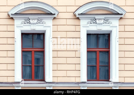 Zwei rechteckigen Fenstern mit einem Gesims in Form eines Bogens von weißem Stuck auf dem Hintergrund einer rosa Wand. Aus einer Reihe von St. Petersburg Fenster Stockfoto