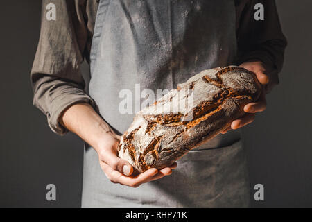 Baker oder Kochen Koch Holding frisch gebackenes Brot auf dunkelgrauem Hintergrund Nahaufnahme. Horizontale. Stockfoto