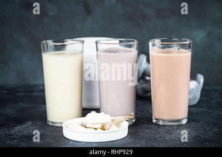 Fitness Concept, Sport Ernährung. Protein Cocktails, Protein Pulver und Hantel. Vanille-, Beeren und Schokolade Protein Shakes. Stockfoto