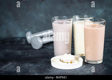 Fitness Concept, Sport Ernährung. Protein Cocktails, Protein Pulver und Hantel. Vanille-, Beeren und Schokolade Protein Shakes. Stockfoto