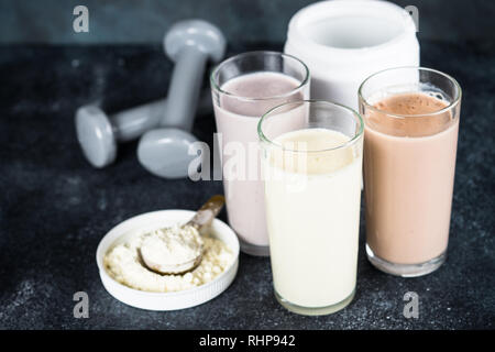 Fitness Concept, Sport Ernährung. Protein Cocktails, Protein Pulver und Hantel. Vanille-, Beeren und Schokolade Protein Shakes. Stockfoto