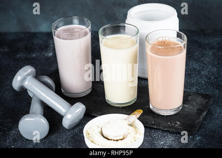 Fitness Concept, Sport Ernährung. Protein Cocktails, Protein Pulver und Hantel. Vanille-, Beeren und Schokolade Protein Shakes. Stockfoto