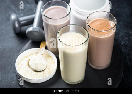 Fitness Concept, Sport Ernährung. Protein Cocktails, Protein Pulver und Hantel. Vanille-, Beeren und Schokolade Protein Shakes. Stockfoto